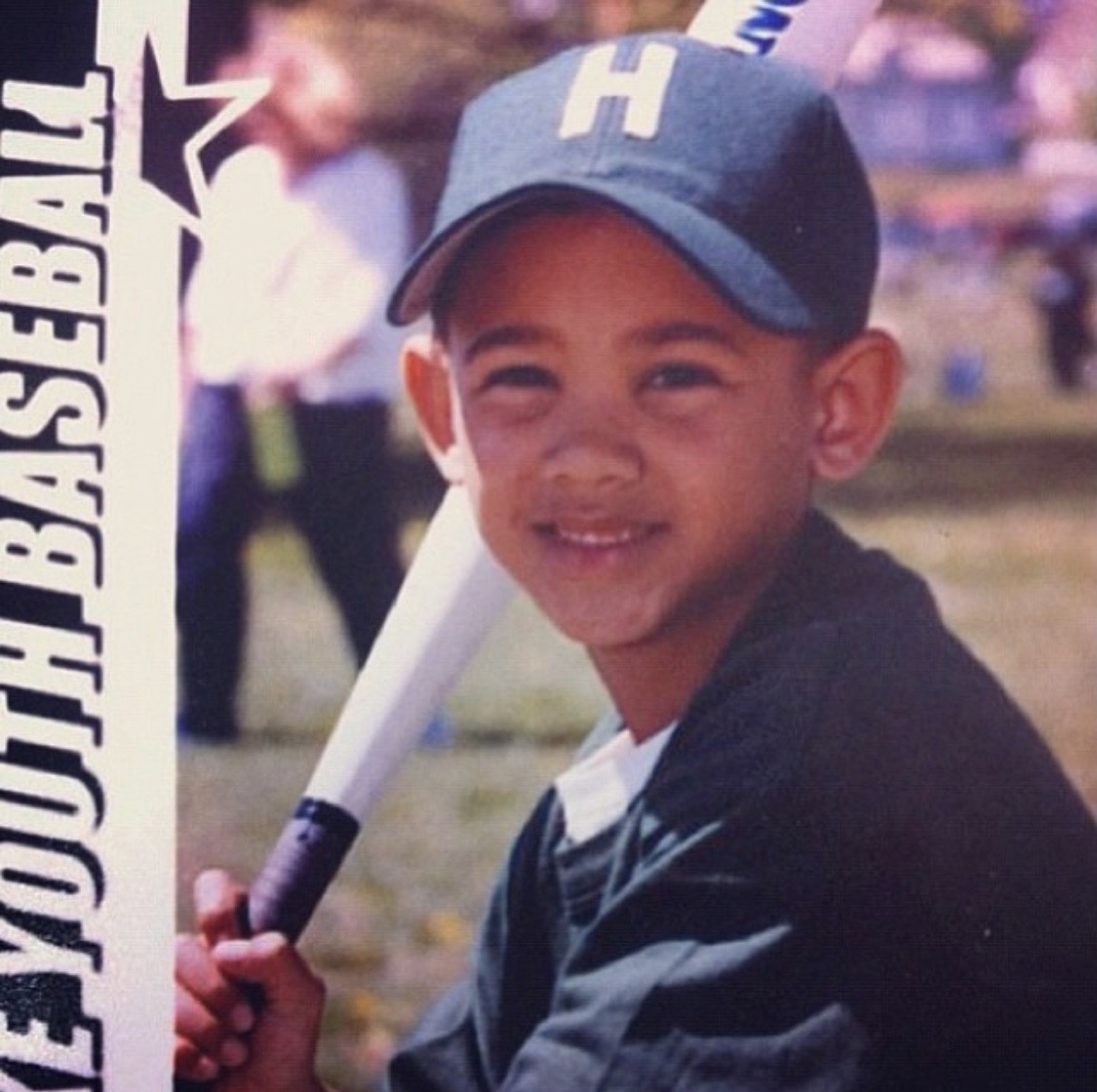 Jamie as a young kid smiling with a bat